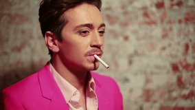 Young man in pink suit with cigarette against scuffed brick wall