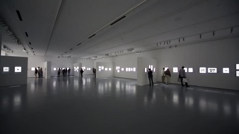 People look at photos at exhibition in large dark gallery