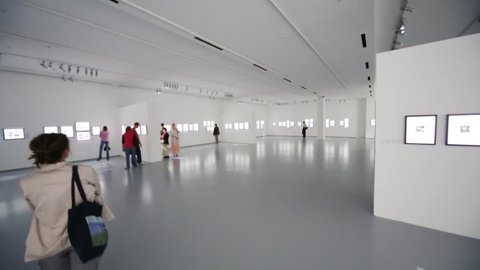 People walk on photo exhibition in large grey gallery