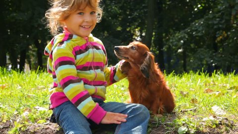 little girl stroking dog in park, looking each other 