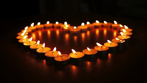 Circular, shallow depth of field, dolly shot of many candles romantically  arranged into a heart.