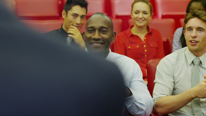 Cheerful diverse business team attending a business presentation or training seminar in company lecture theatre.