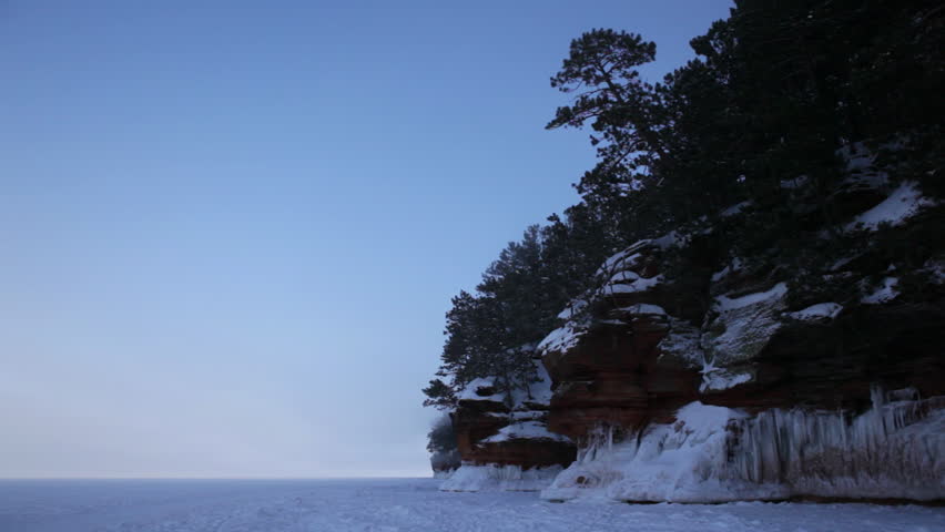 The Apostle Island mainland sea caves as ice caves on frozen Lake Superior, Wisconsin, Midwest USA. Profile of a icy tree-covered cliff with ice caves below and flat expanse of open lake behind.
