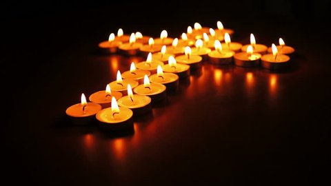 Circular, shallow depth of field, dolly shot of many candles  arranged into a spiritual cross.