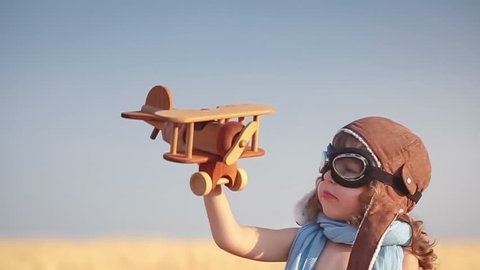 Happy kid playing with toy vintage airplane against summer blue sky background. Travel concept. Slow motion