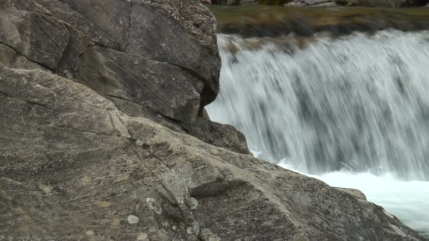 HD 1080i: Close-up of the legs and feets of an mountaineer ascending a rock at a river. Tripod.