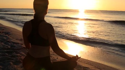 Silhouette of a woman meditating at the beach at sunrise