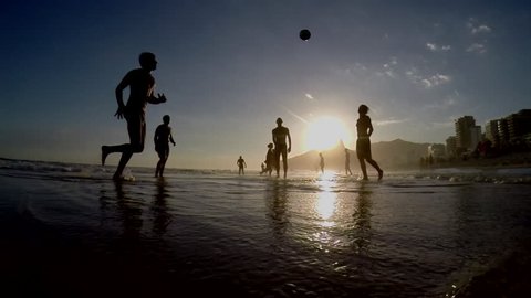 Silhouettes of Carioca Brazilians playing beach football at sunset on Ipanema Beach Rio de Janeiro Brazil silhouetted slow motion