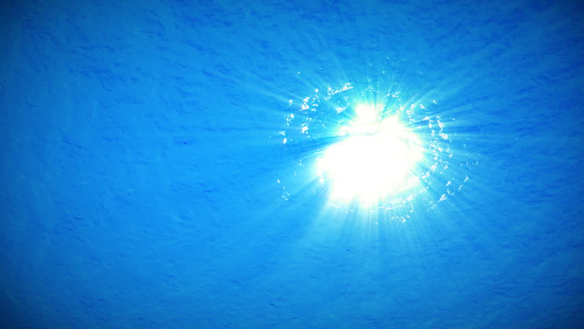 An underwater clip of a calm ocean surface with sunlight shining down through