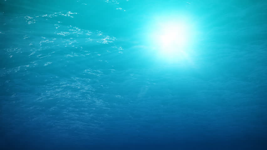 An underwater clip of a calm ocean surface with sunlight shining down through