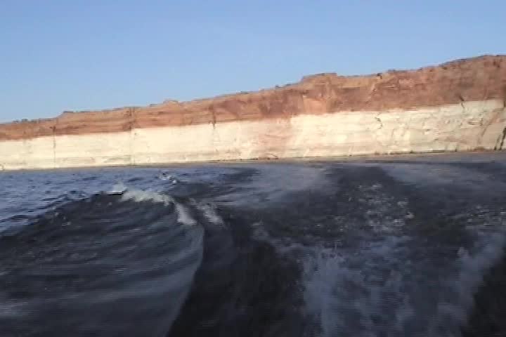 The wake of a boat with the shore of Lake Powell in the background--cliff shows normal water line