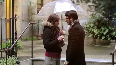 first kiss - a man kisses a woman under an umbrella in the rain