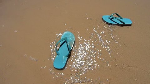 Wave comes in and washes a pair of flip flops into the beach.