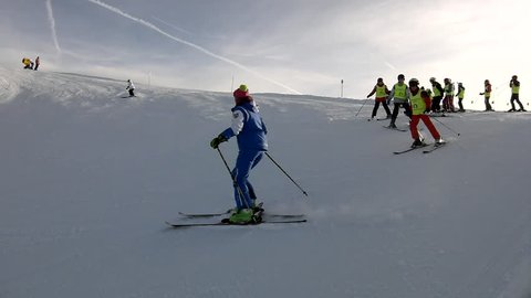 Peak of mountain with slope for downhill skiing in Alps ski resort, bunch of skiers from ski school enjoying fresh powder snow on slope. Sunny winter day in Alps.