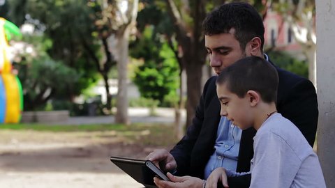 Father and his little son relaxing and looking at laptop screen in park