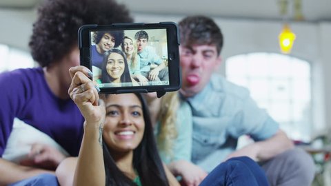 Happy and casual group of young friends at home, posing to take a photograph of themselves with a computer tablet. 