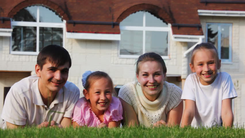 family with two little girls lies on lawn and smiles 