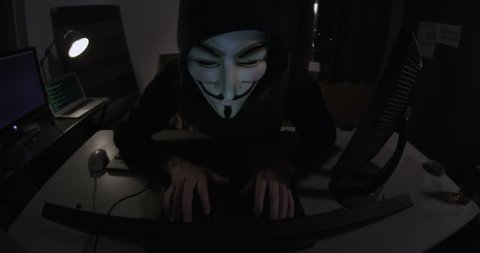 NEW YORK, NY, USA - CIRCA 2013: A hacker activist sits at their laptop computer in a grungy apartment. They are wearing a Guy Fawkes mask which has become an iconic symbol of online social movements