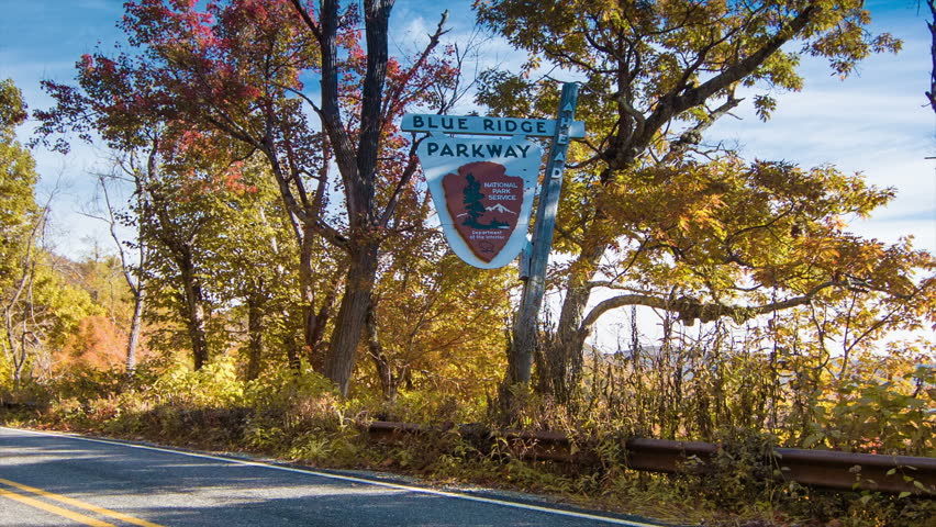 Family Sedan Passing a Nostalgic Blue Ridge Parkway Sign near Asheville, NC in the Fall with Autumn Colored Trees and a Blue Sky in the Appalachian Mountains of Western North Carolina. Sound Included.