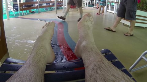 Mans hairy legs feet cruise ship swimming area. Pool fun cruise ship Caribbean. Outdoor lounge and bar above swimming pool. Luxury cruise ship vacation in Caribbean Ocean.