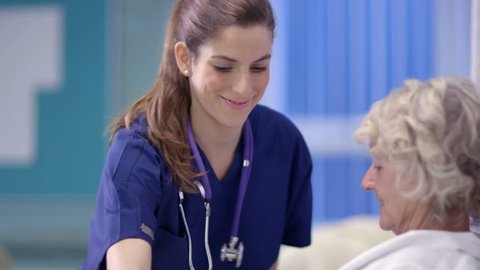 Caring nurse chats with a female patient on a hospital ward.