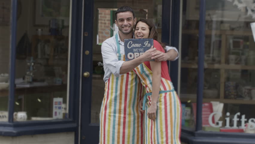 Happy business partners outside a shop hold up a sign to show they are open