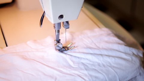 A woman sitting at a table sewing clothes on a sewing machine.