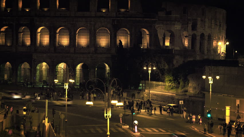 Vehicles and pedestrians in front of Colosseum at night