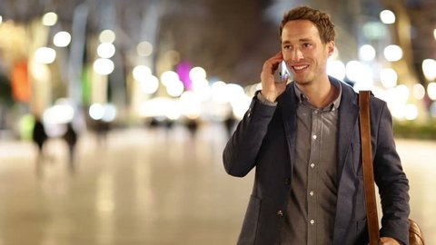 Smart phone man calling on mobile phone at night on La Rambla in Barcelona, Spain. Handsome young business man talking on smartphone and walking away smiling happy wearing suit jacket outdoors.