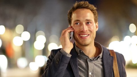 Smart phone man calling on mobile phone at night in city. Handsome young business man talking on smartphone smiling happy wearing suit jacket outdoors. Urban male professional in his 20s.