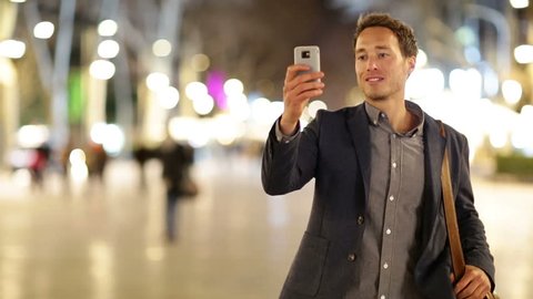 Man taking photo with camera phone at night on La Rambla, Barcelona, Spain. Young casual man taking picture with camera phone outside.