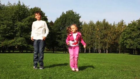 Boy and girl jumps on field before trees 
