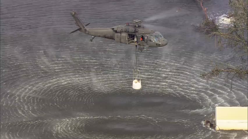 Flood Water Rescue Aid Helicopter Hurricane Barricade. Helicopter dropping an anti flood barricade in water below.