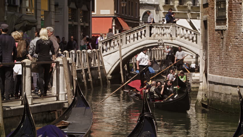 VENICE, ITALY - MAY 2, 2012: Gondolier steer's gondola under a bridge.