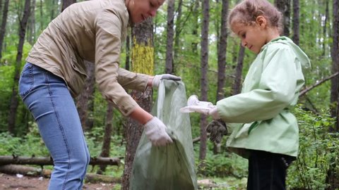 Mother with daughter helping clean up green forest