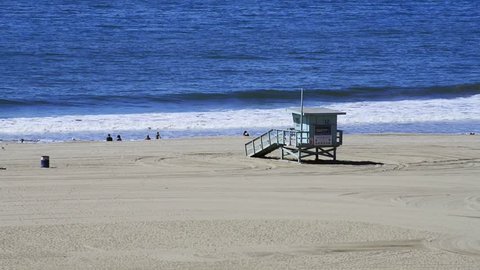 Panoramic of Santa Monica's beach during winter, with very few people enjoying the ocean during a sunny day, close to a lifeguard tower 