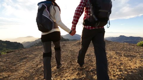 Couple holding hands hiking outdoors at romantic sunset. Hikers man and woman lovers trekking walking with backpacks in trail at sunset in mountains by Roque Nublo, Gran Canaria, Canary Islands, Spain
