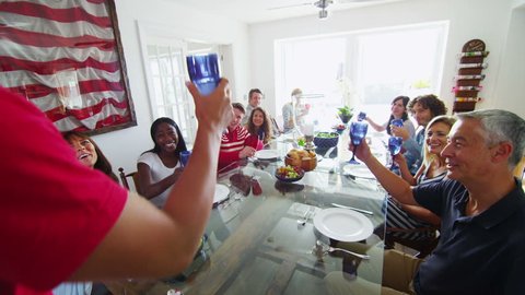 Happy diverse group of family and friends, sitting at a table before a meal raise their glasses for a toast. In slow motion. Stock-video