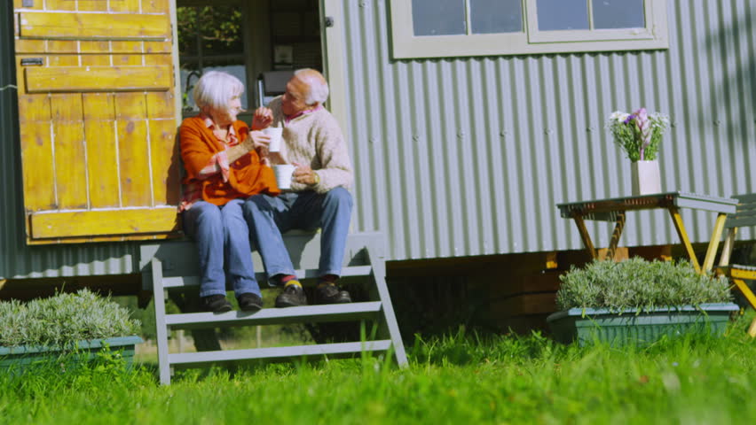 Cheerful senior couple relaxing outside quaint traditional caravan on a bright autumn day.