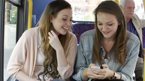 Two young girls sitting on bus reading text message and laughing.Shot on Sony FS700 in PAL format at a frame rate of 25fps