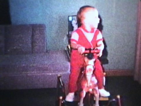 A little boy has fun riding his new bouncy horse in the living room. (1963 - Vintage 8mm film)
