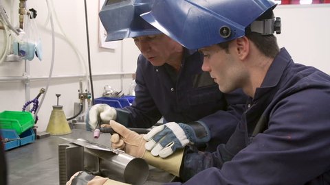 Engineer explaining to apprentice how to use TIG welding machine before they both lower protective face masks.Shot on Sony FS700 in PAL format at a frame rate of 25fps