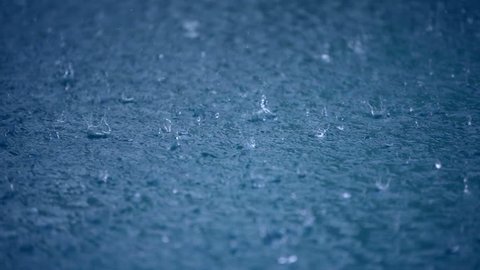 Raining water blue background, drops to puddle surface, wet weather, abstract liquid nature closeup video. Raindrop falling season. Splash, ripple on the road in rainy city, dark heavy storm outdoors.