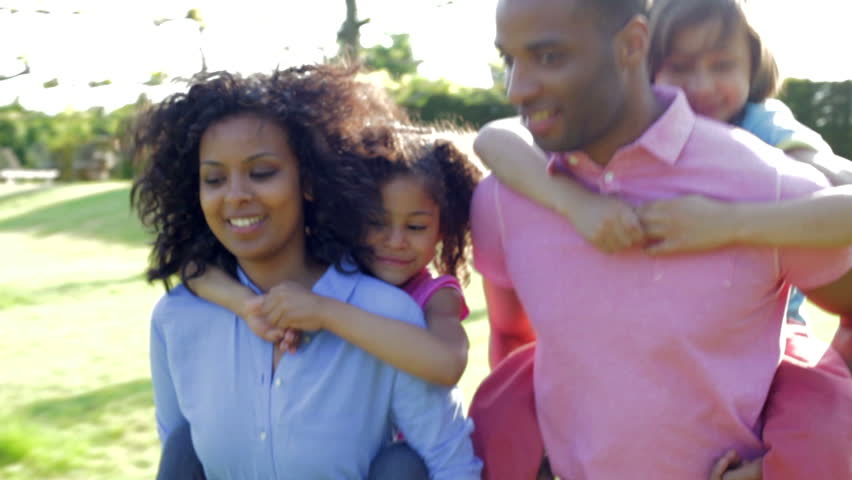 African American family walking along country track with children riding on parents backs.Shot on Canon 5d Mk2 with a frame rate of 25fps