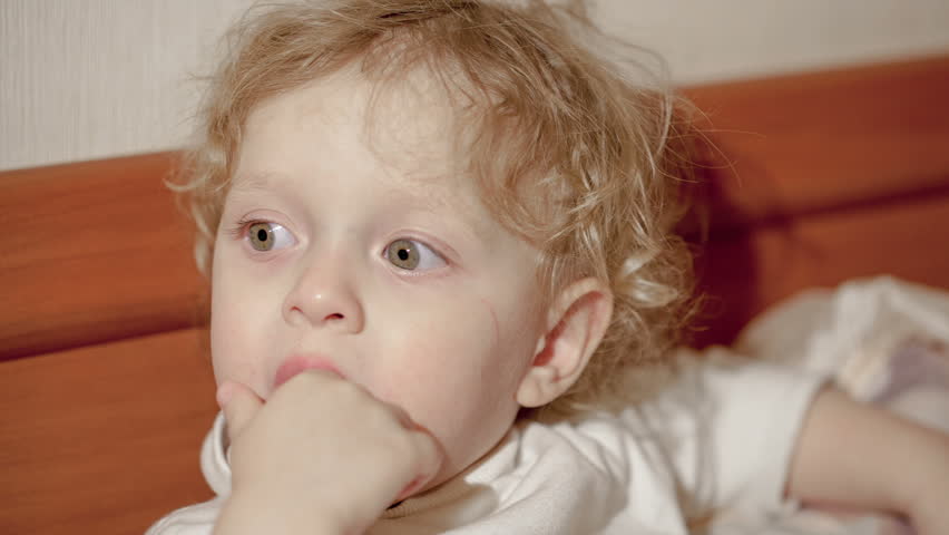 Close-up shot of little boy on bed looking somewhere with his fingers in the mouth