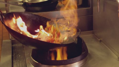 Chef tossing flaming stir fry in slow motion