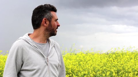 Male model with authentic look wearing casual cloths 
stand in a meadow, smiling to the camera.
Background of yellow wild flowers and cloudy skies