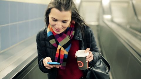 Young woman with smartphone and coffee riding escalator
