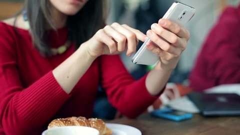 Woman hands texting on smartphone and eating croissant in cafe
