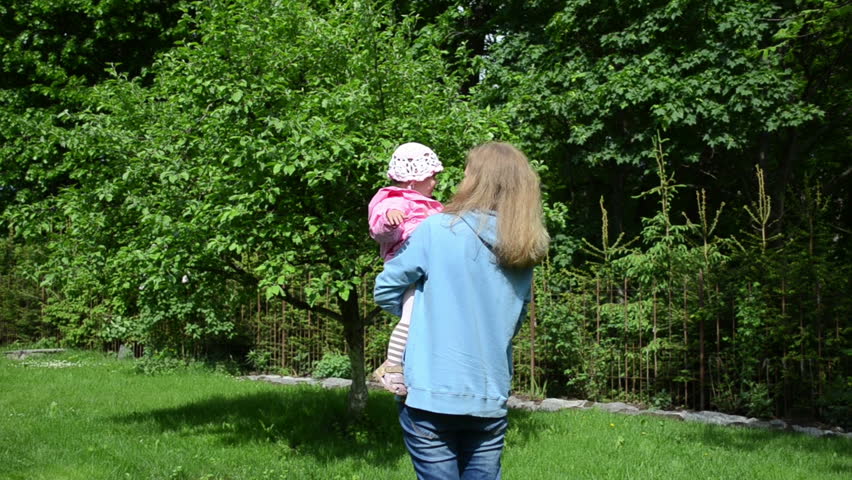 blonde woman with blue jumpers on the hands keep child goes to the apple tree in the garden